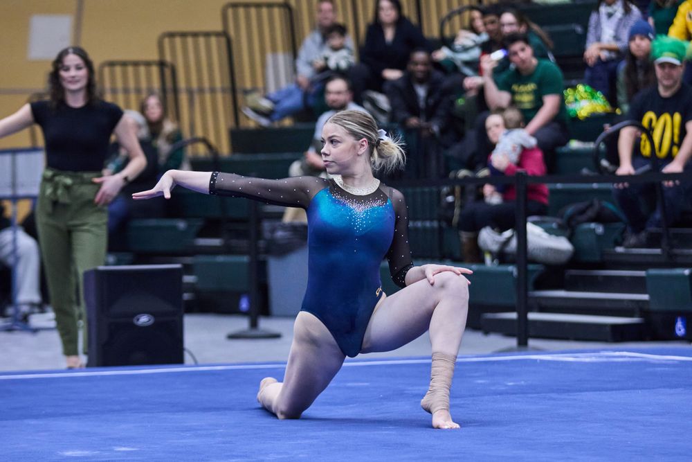 Gymnast in blue leotard executes floor routine move at competition.