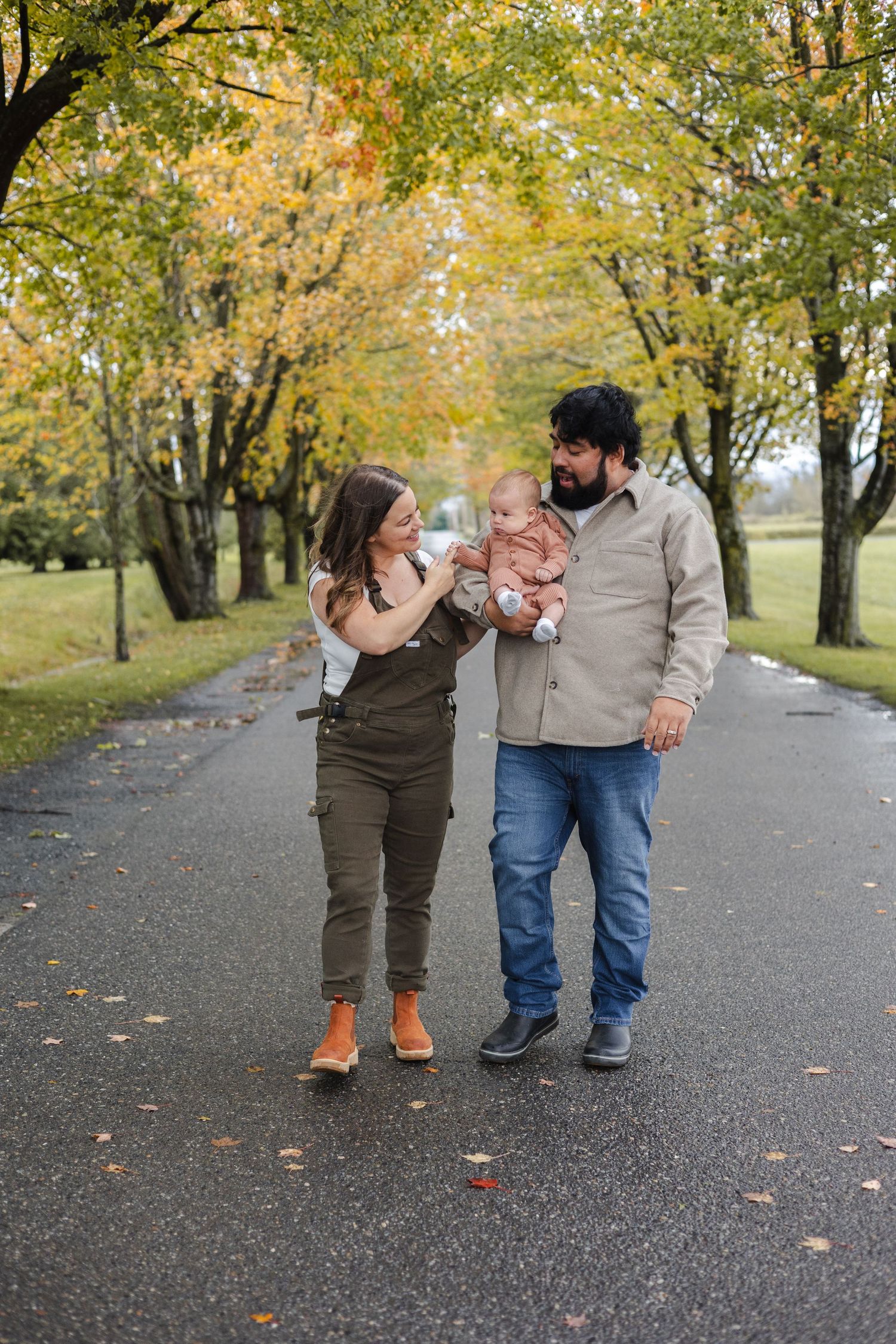 Family walking together on tree-lined autumn path with fallen leaves.