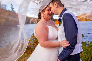 Bride and groom share a romantic moment under a flowing veil by a lake with autumn foliage. Nova Scotia wedding  Cape Breton