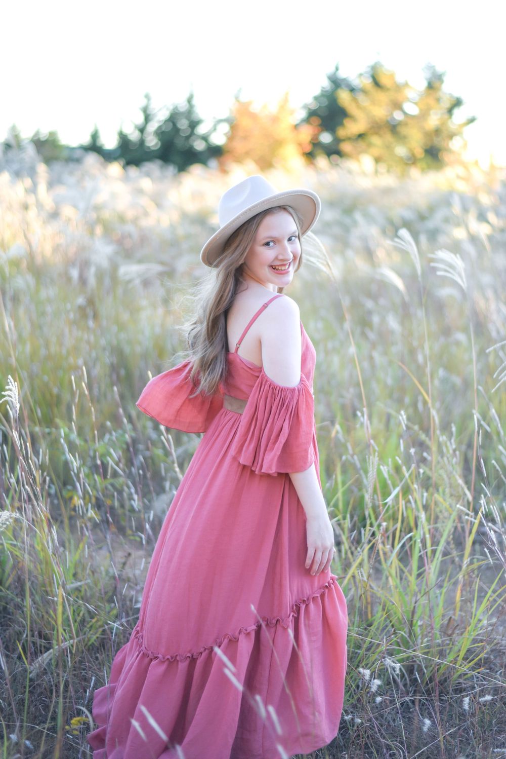 Pink dress and sun hat create dreamy summer portrait in golden field.