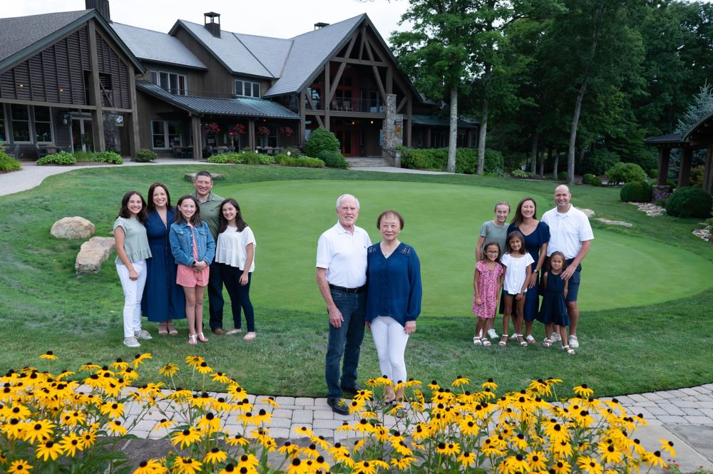 Group gathered on a lush lawn in front of a rustic lodge with yellow flowers blooming in the foreground.