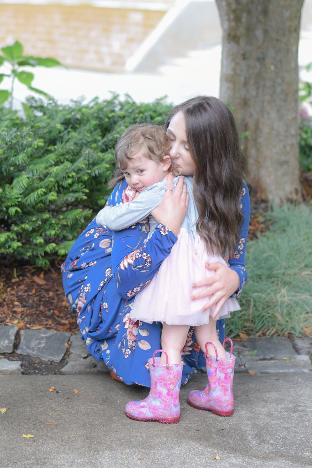 Pink rain boots and floral dress create playful moment in garden setting.