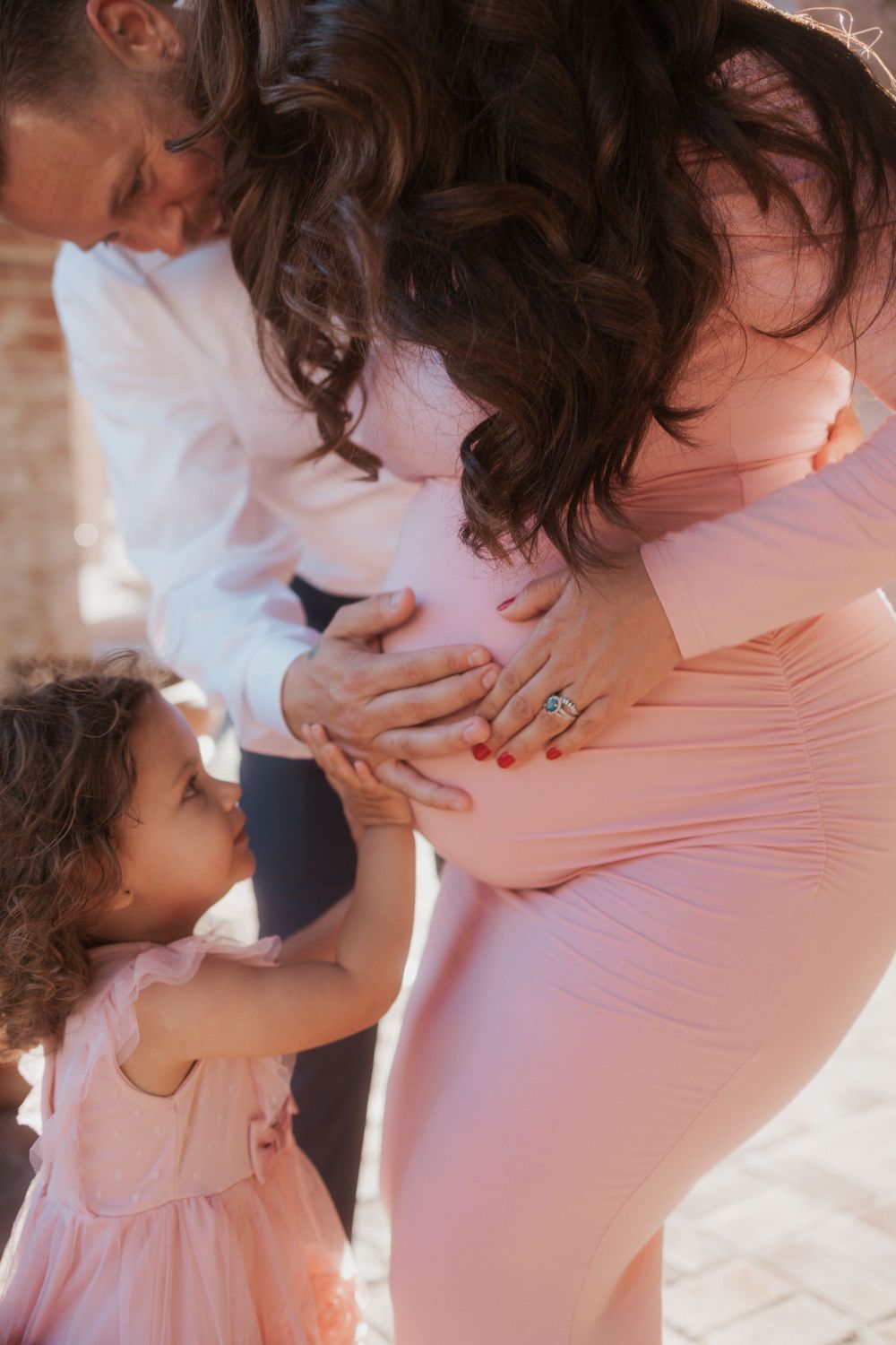 An intimate maternity photo showing hands touching a pregnant belly in a pink dress.