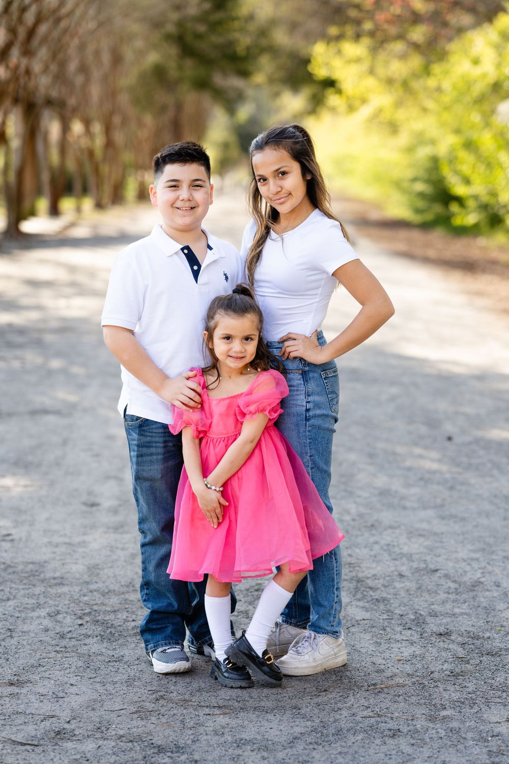 A family portrait on a wooded path with coordinated white and pink outfits.