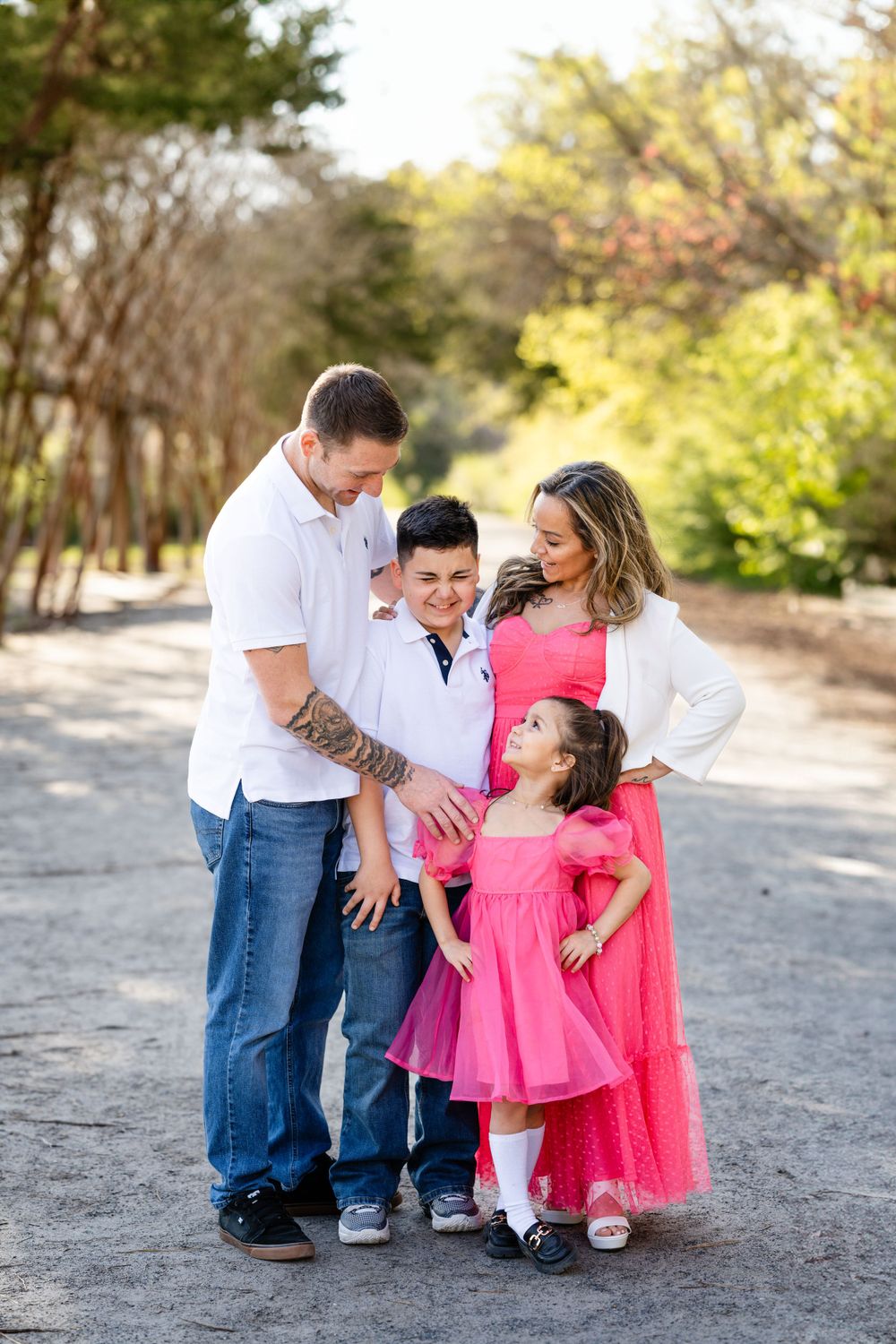 A casual family photo session on a tree-lined path with coordinated pink and white outfits.