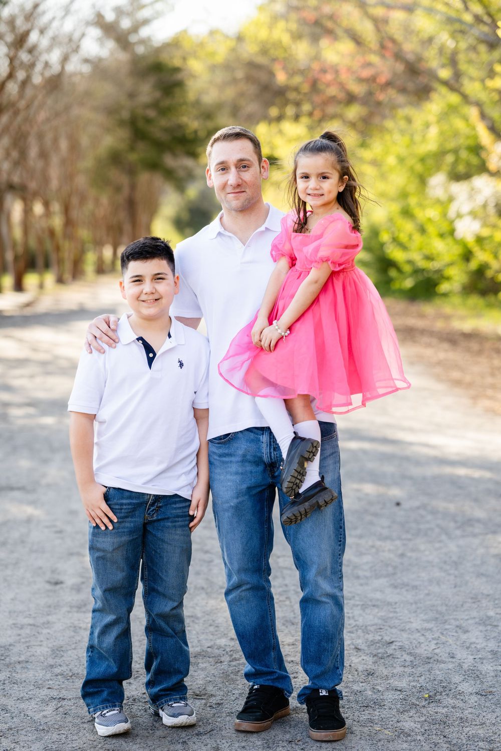 A family of three dressed in casual attire poses together on a peaceful wooded path.