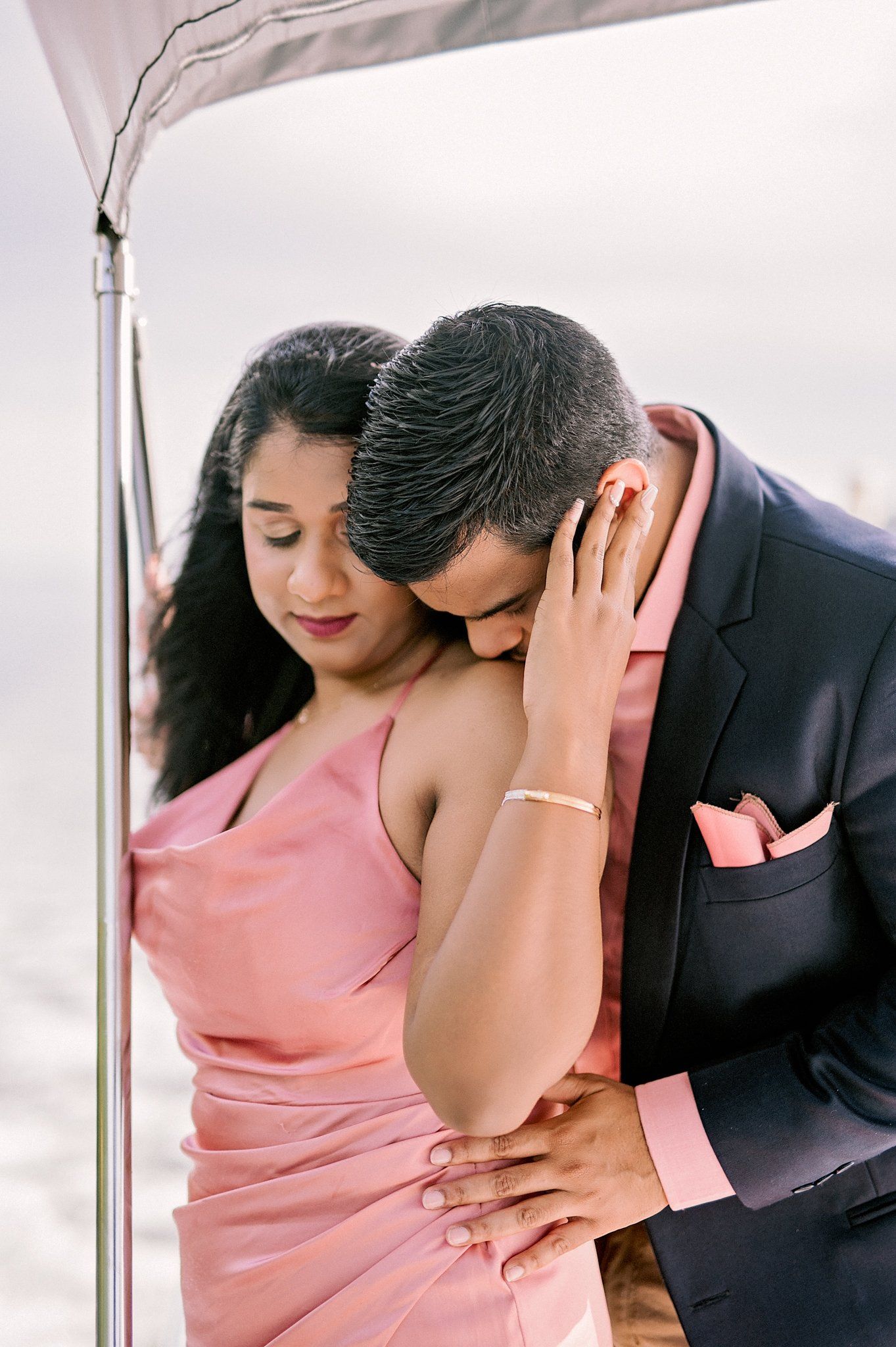 Romantic couple in formal attire sharing intimate moment under outdoor canopy.