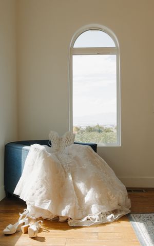 Elegant lace wedding gown draped over a chair near an arched window with a scenic outdoor view.