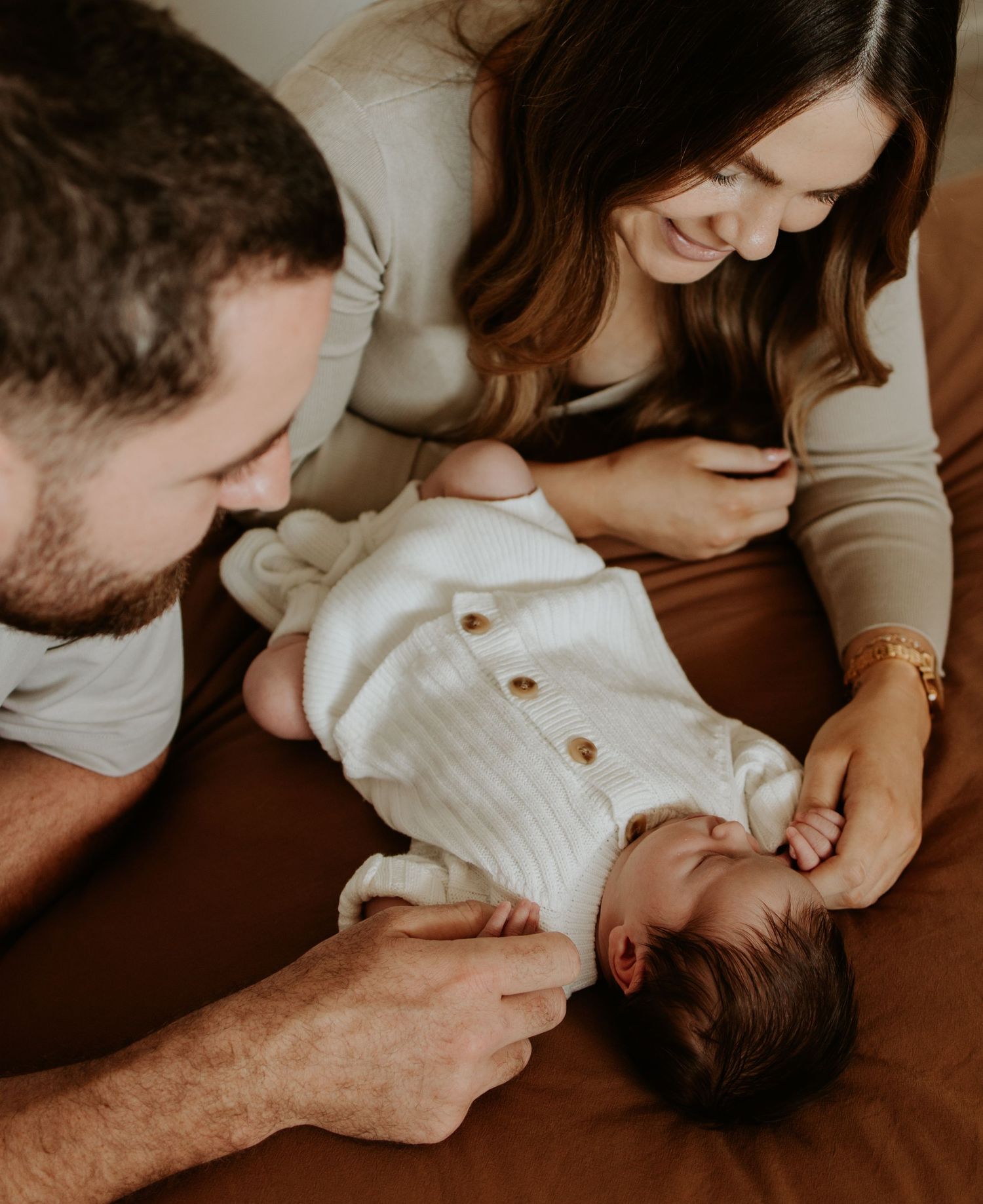 A series of intimate family moments captured during a newborn photo session in warm, moody lighting.