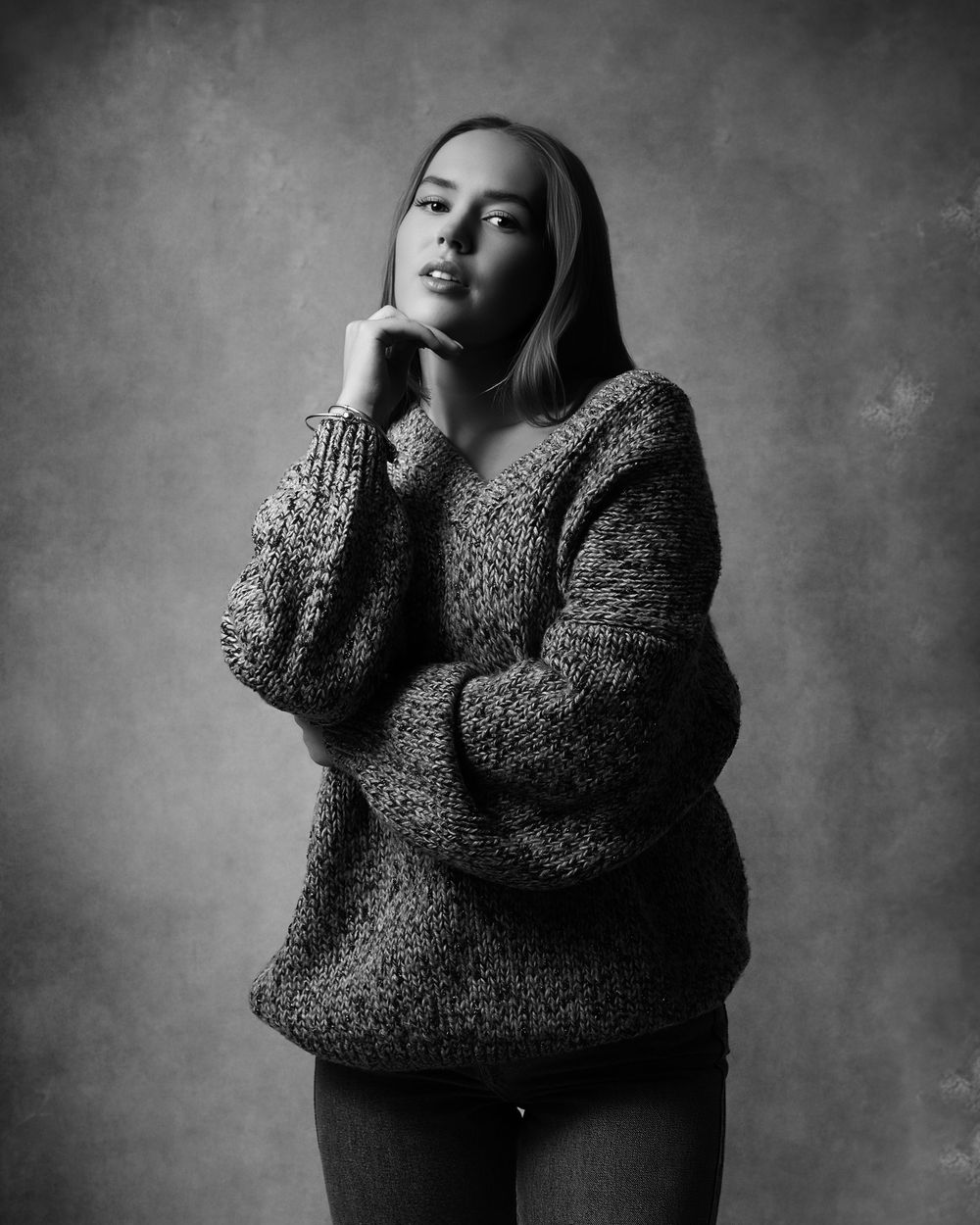 Artistic black and white portrait of someone in a cozy knit sweater with thoughtful pose against textured background.