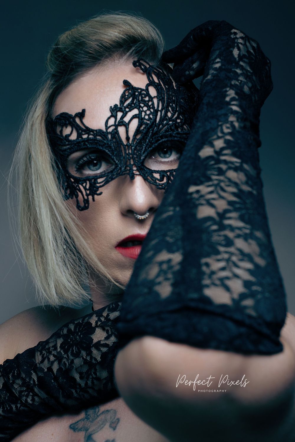 Artistic portrait featuring an ornate black lace masquerade mask and matching gloves against a dark background.