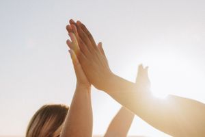 Silhouetted hands raised against bright sunlight in celebration.