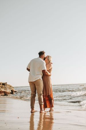 A couple shares an intimate moment while standing in shallow ocean water at sunset.
