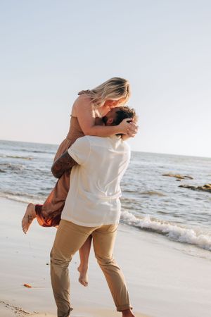 A playful couple spins and dances together on a sunlit beach.