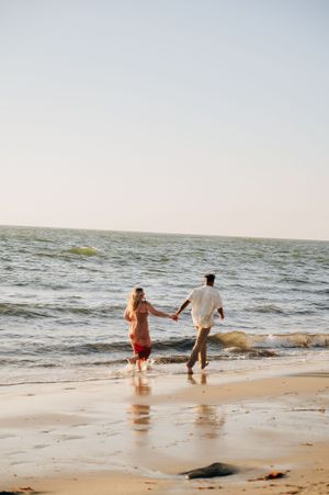 A couple runs together along the beach shoreline at sunset.