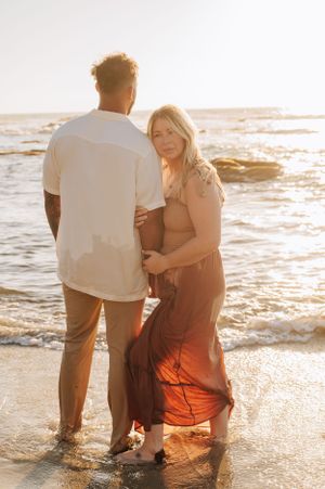 A couple shares an intimate moment on the shoreline during golden hour.