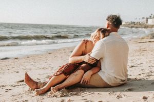 Side view of couple relaxing on beach sand during golden hour.