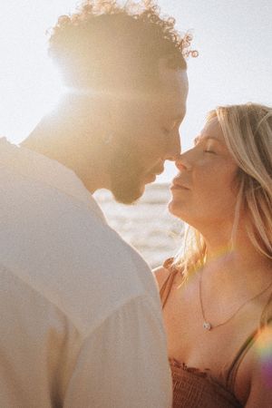 Sun-drenched profile portrait of couple in intimate moment at beach.