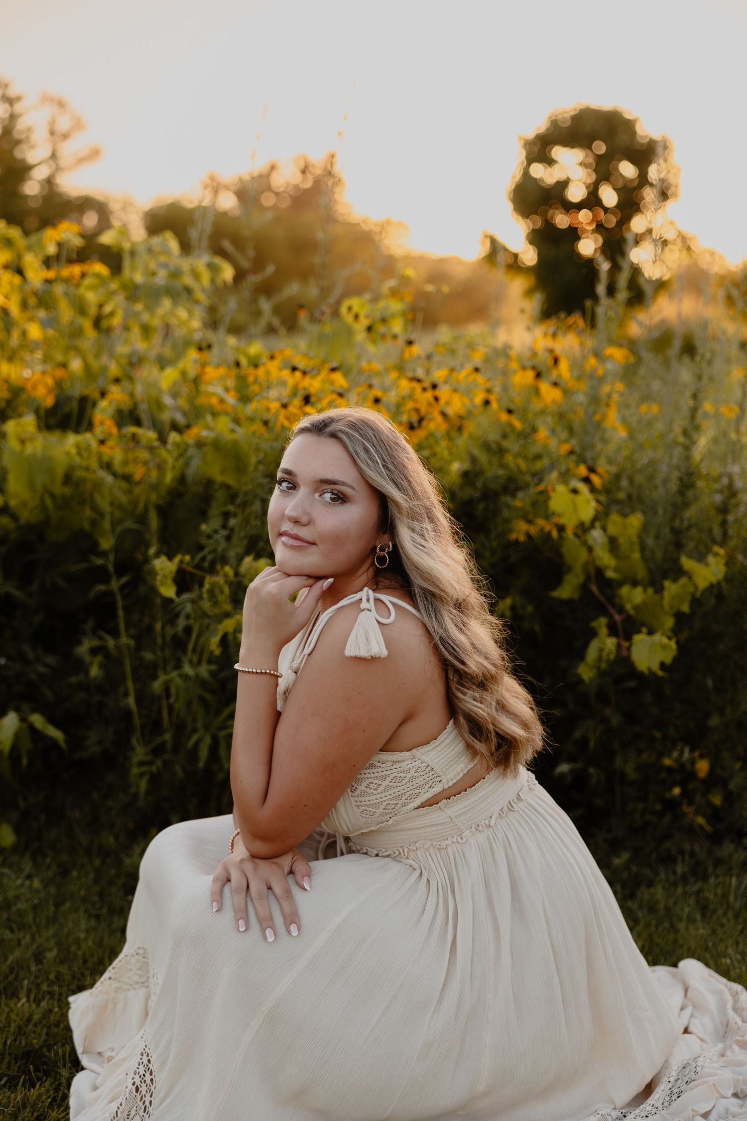 Senior in a flowing white dress poses gracefully in a field of wildflowers at sunset in Brookfield, WI  with Essence Rose Photography.