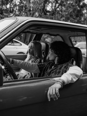 Two people sitting in a parked car captured in black and white vintage-style photography.