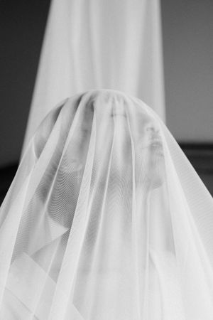 A black and white photograph shows a person covered in a sheer white veil creating an ethereal silhouette effect.