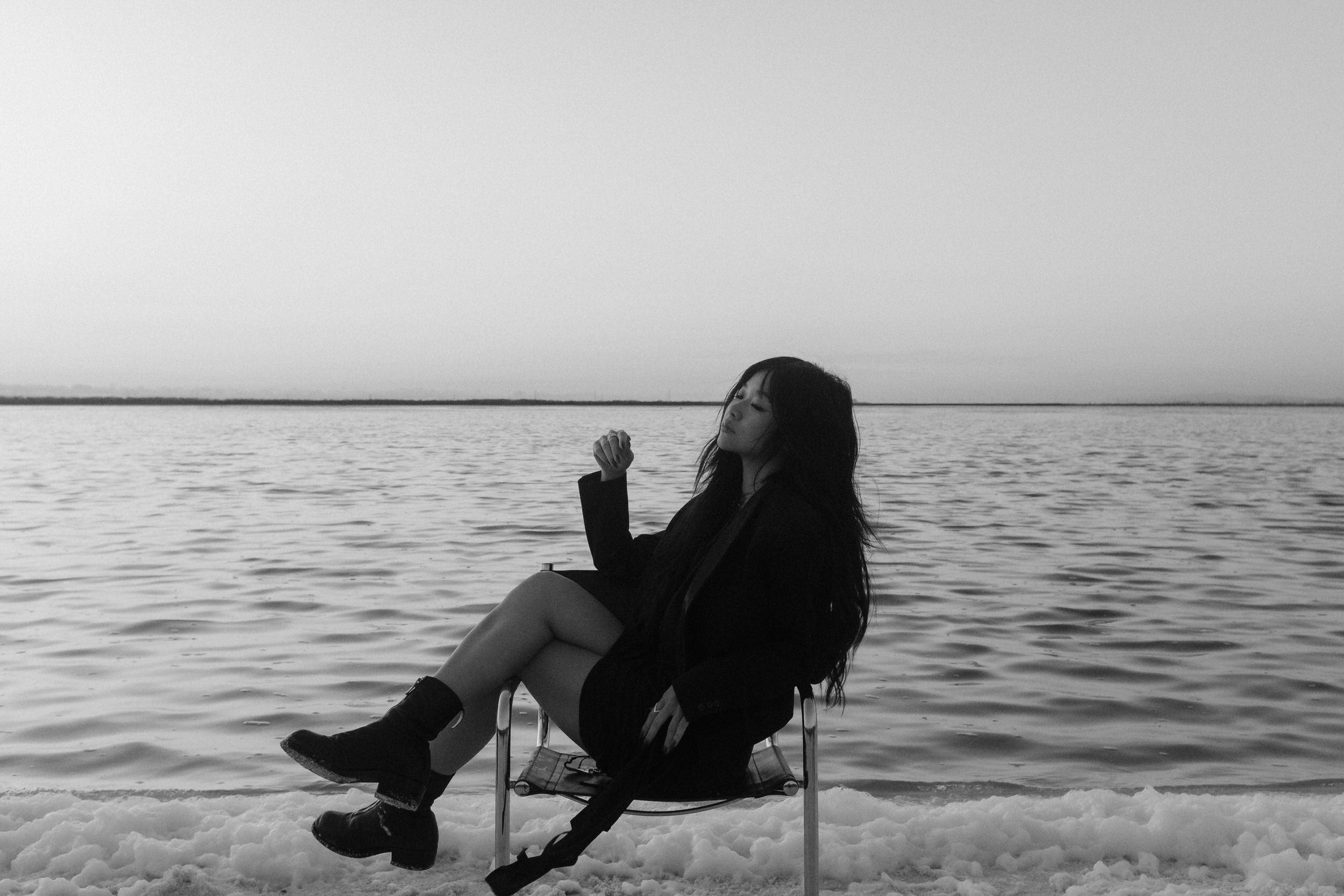 A person relaxes in a chair at the water's edge with a scenic view of a lake or ocean at dusk.