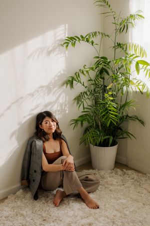 A serene indoor corner with a large potted palm plant casting shadows on white walls and carpet.