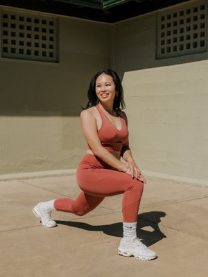 Person in coral-colored athletic wear doing lunges on concrete patio while wearing white chunky sneakers and socks.