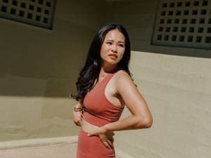A person in a coral athletic set strikes a confident pose against a beige wall in warm sunlight.