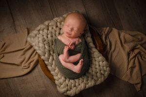 A peaceful sleeping newborn on a chunky knit blanket in warm earth tones.