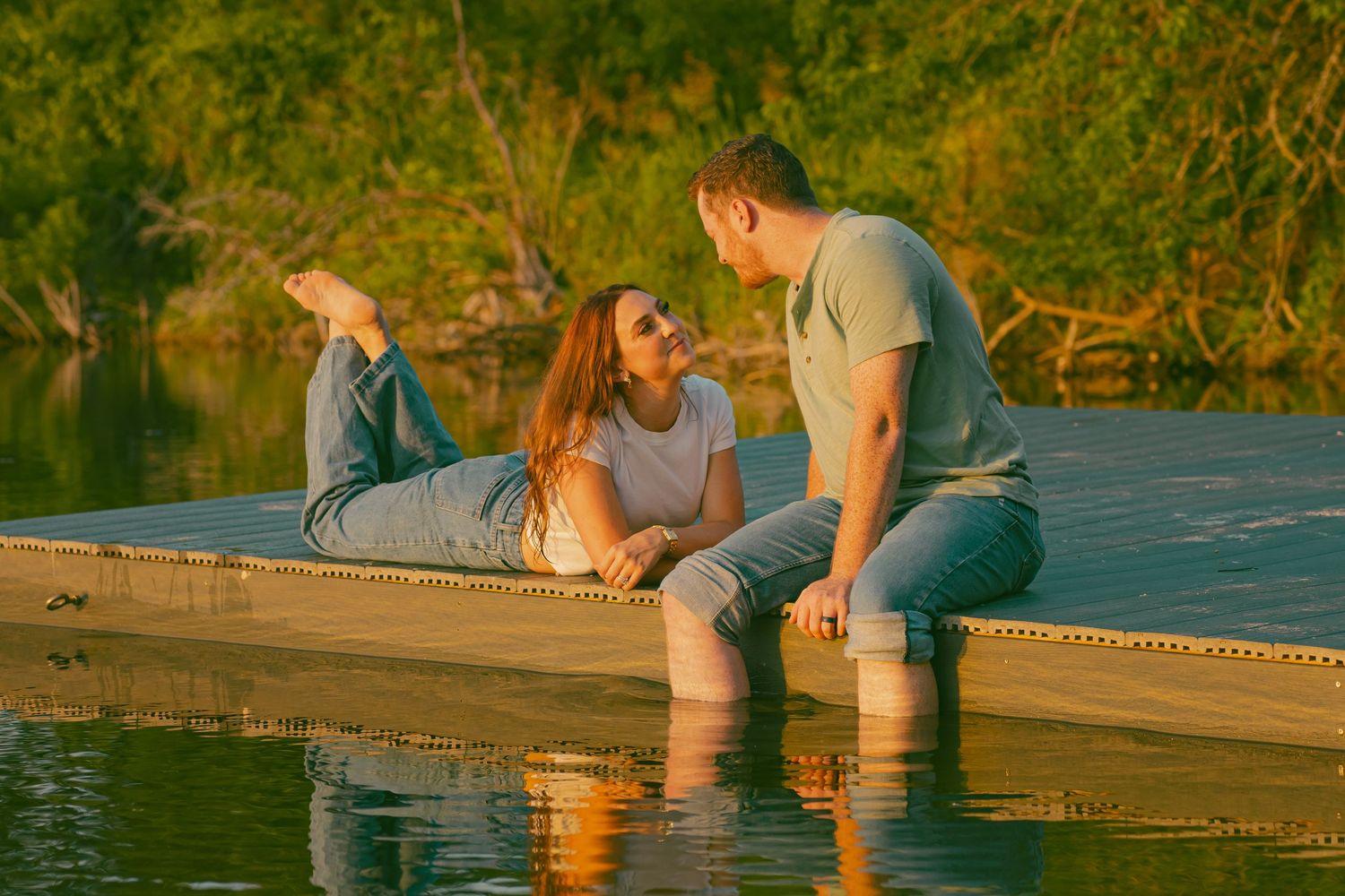 Couple relaxing on wooden dock by lake during golden hour sunset.