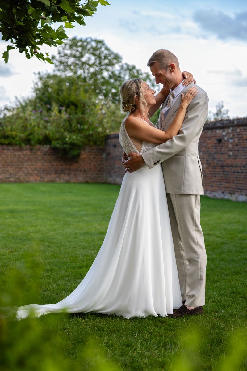 A tender embrace between newlyweds on a manicured lawn with brick wall background.