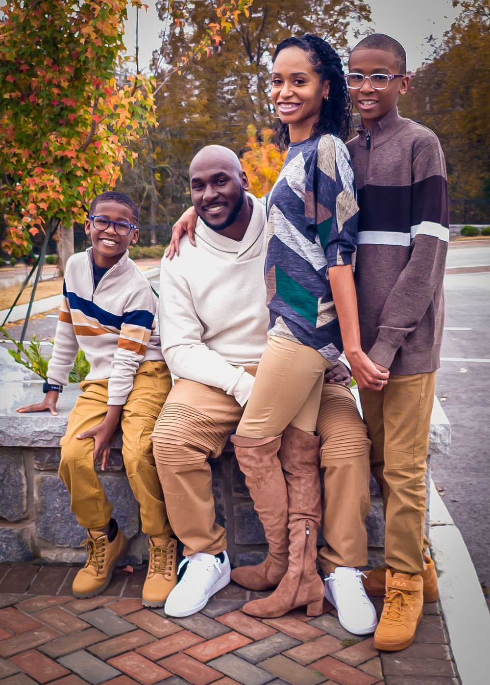 A family wearing coordinated sweaters poses together on brick steps during autumn.
