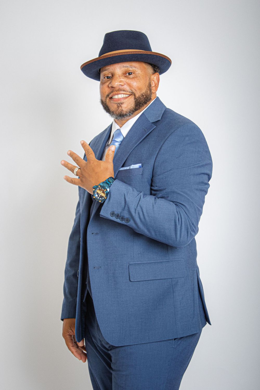 Stylish person in blue suit and navy fedora poses confidently against light background.