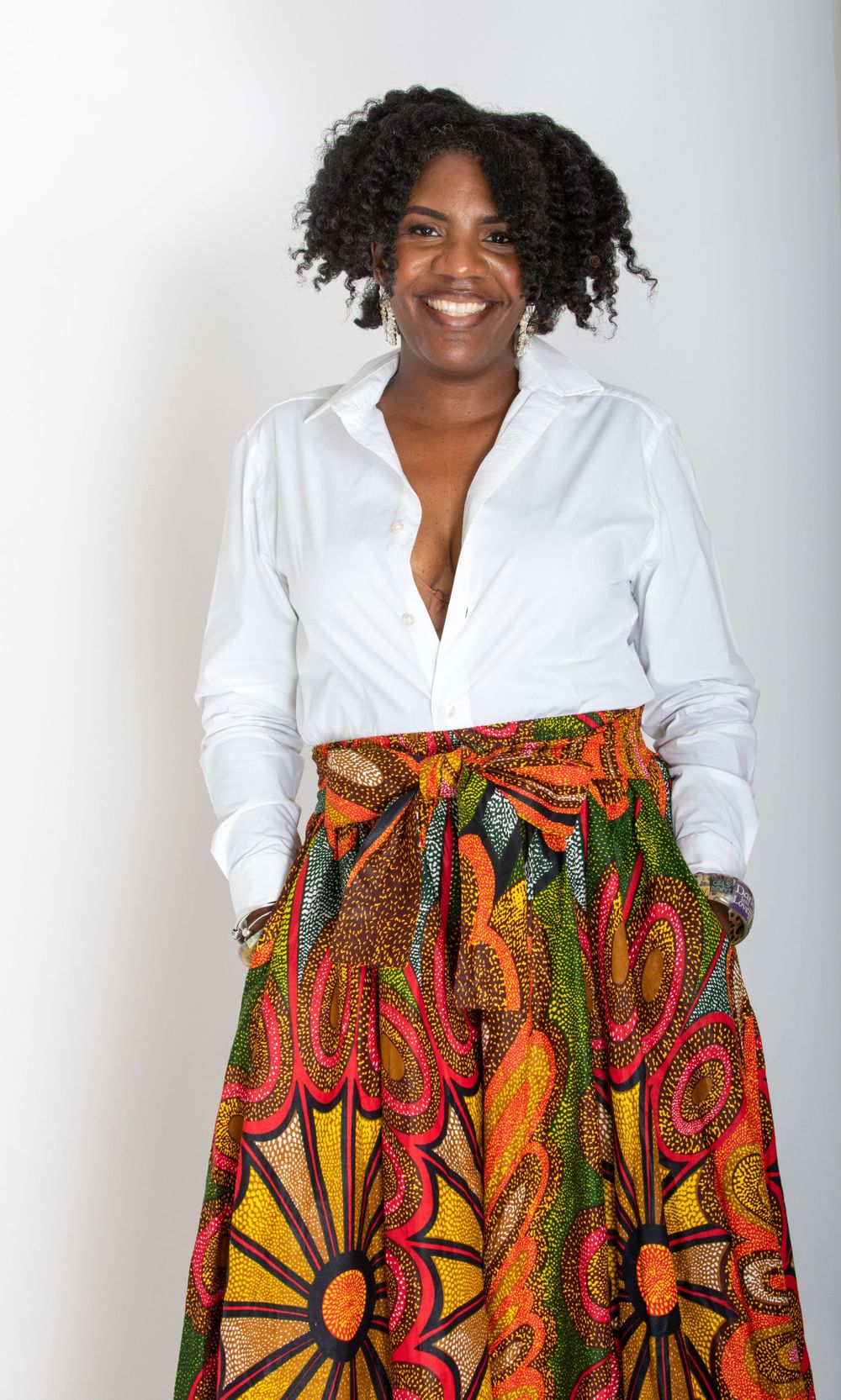 Person in white button-down and vibrant printed skirt poses confidently.