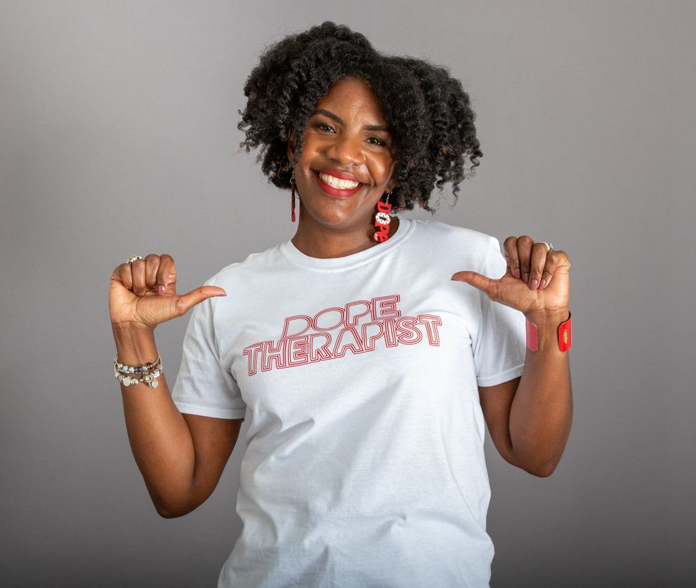 Person in white t-shirt points to text on shirt while posing against grey background.
