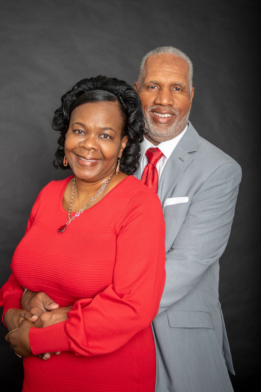 Formal studio portrait of couple in red and gray against dark background.