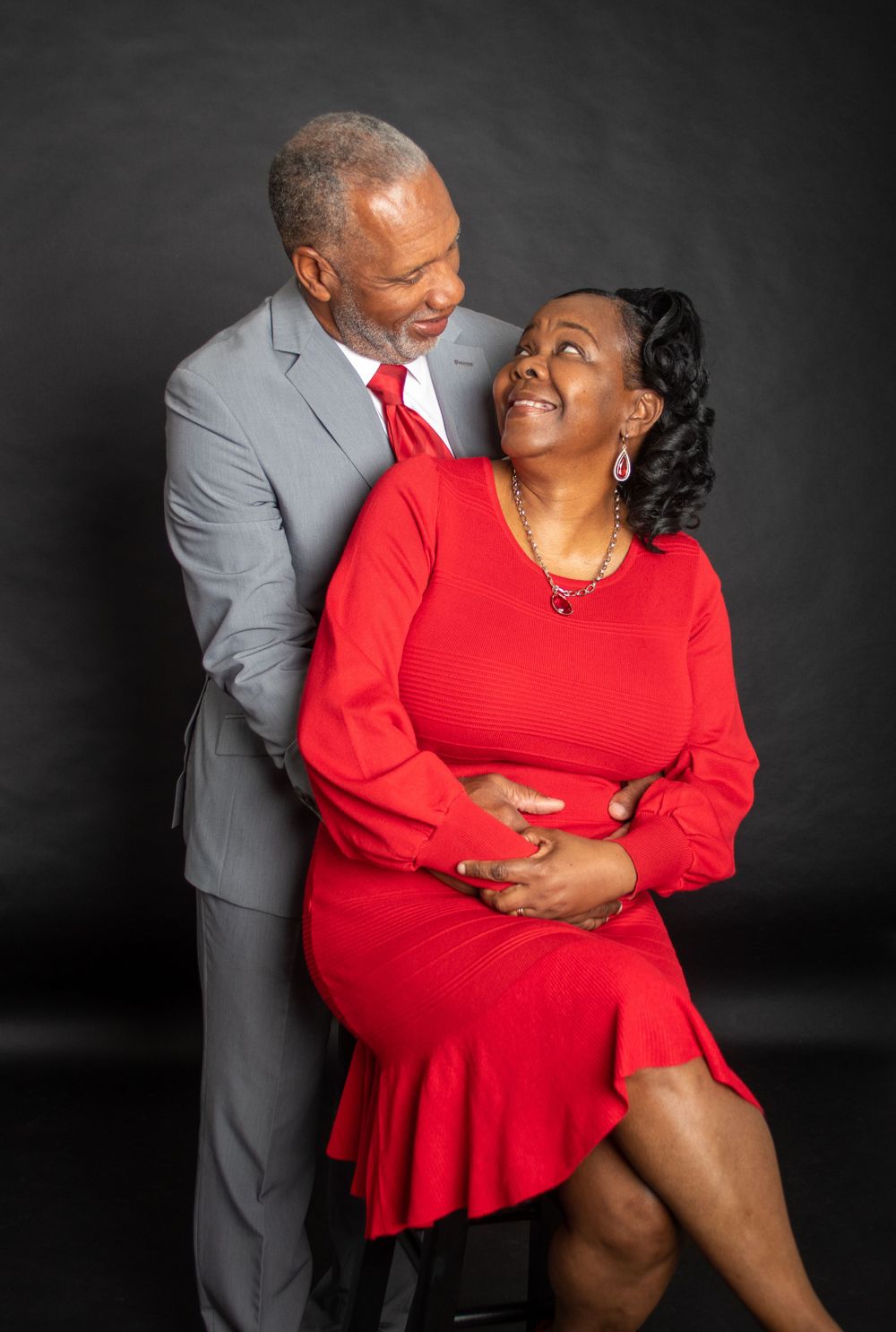 Romantic studio portrait of couple embracing in formal attire against dark backdrop.