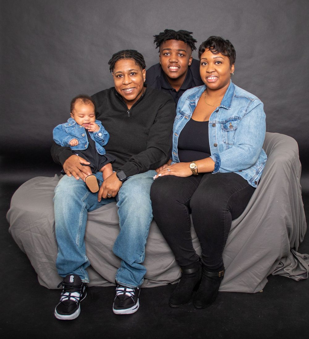 Family of four poses together on gray couch for studio portrait.