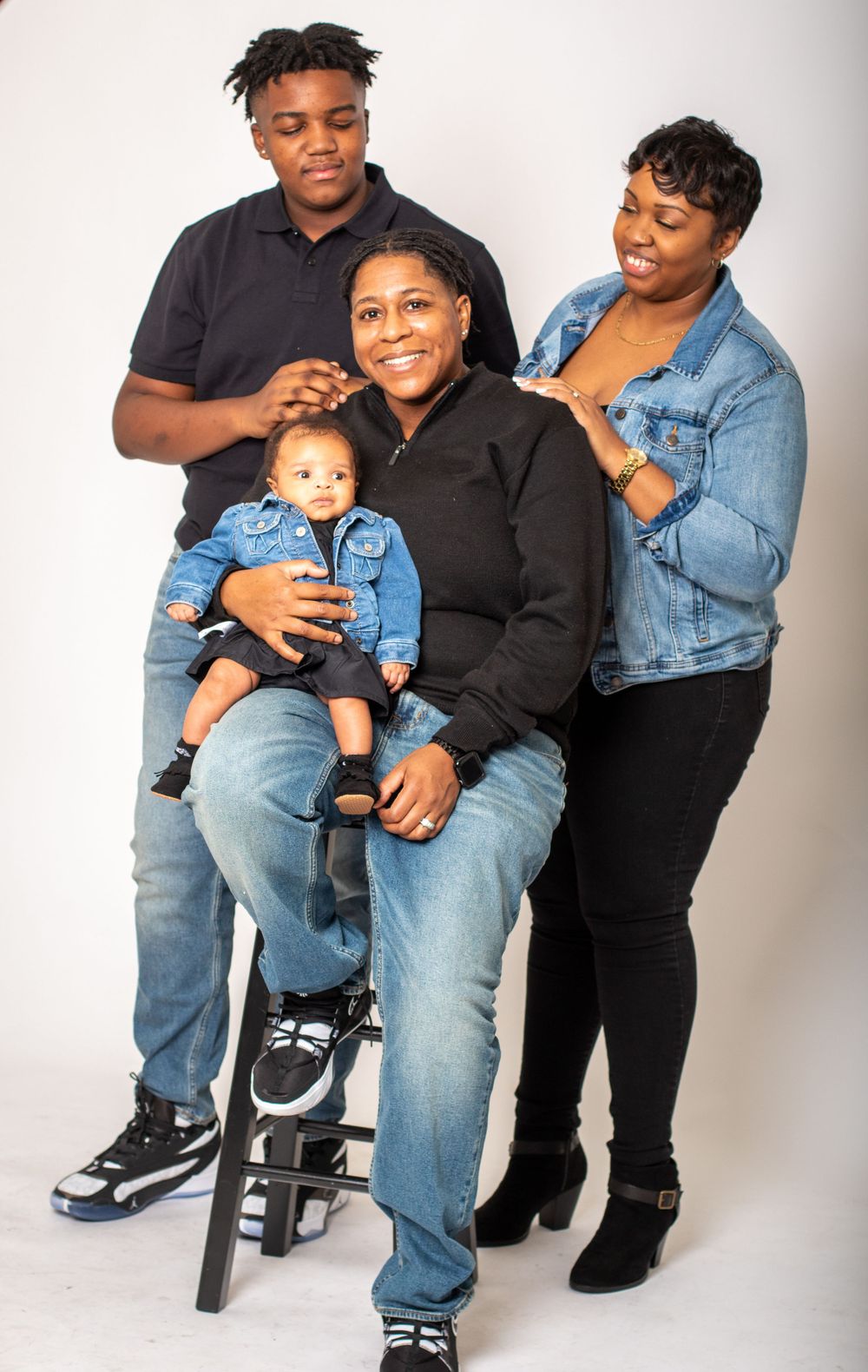 Family portrait showing group in coordinating denim outfits against white background.