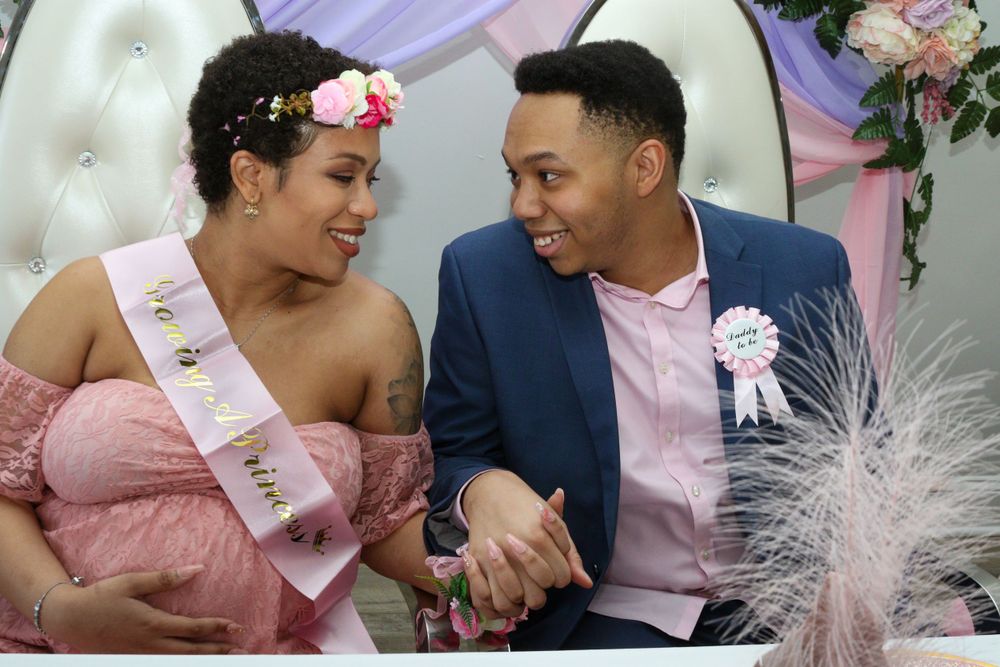 A couple shares an intimate moment at a baby shower with pink decor and balloons.