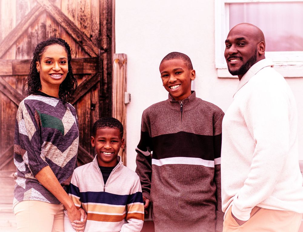 A family of four poses together in casual wear against a wooden door background.