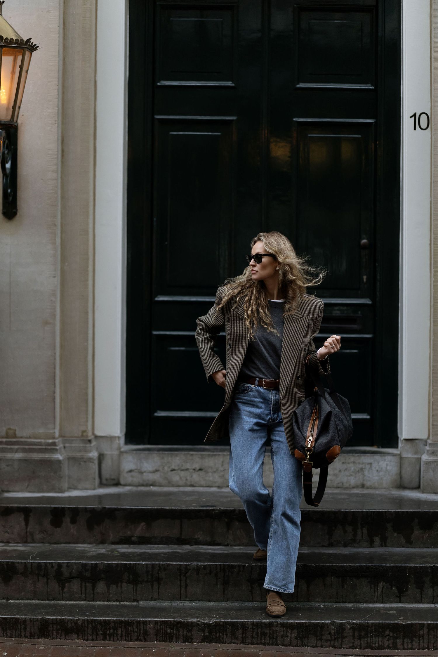 Stylish woman in blazer and jeans descending steps outside classic black door.