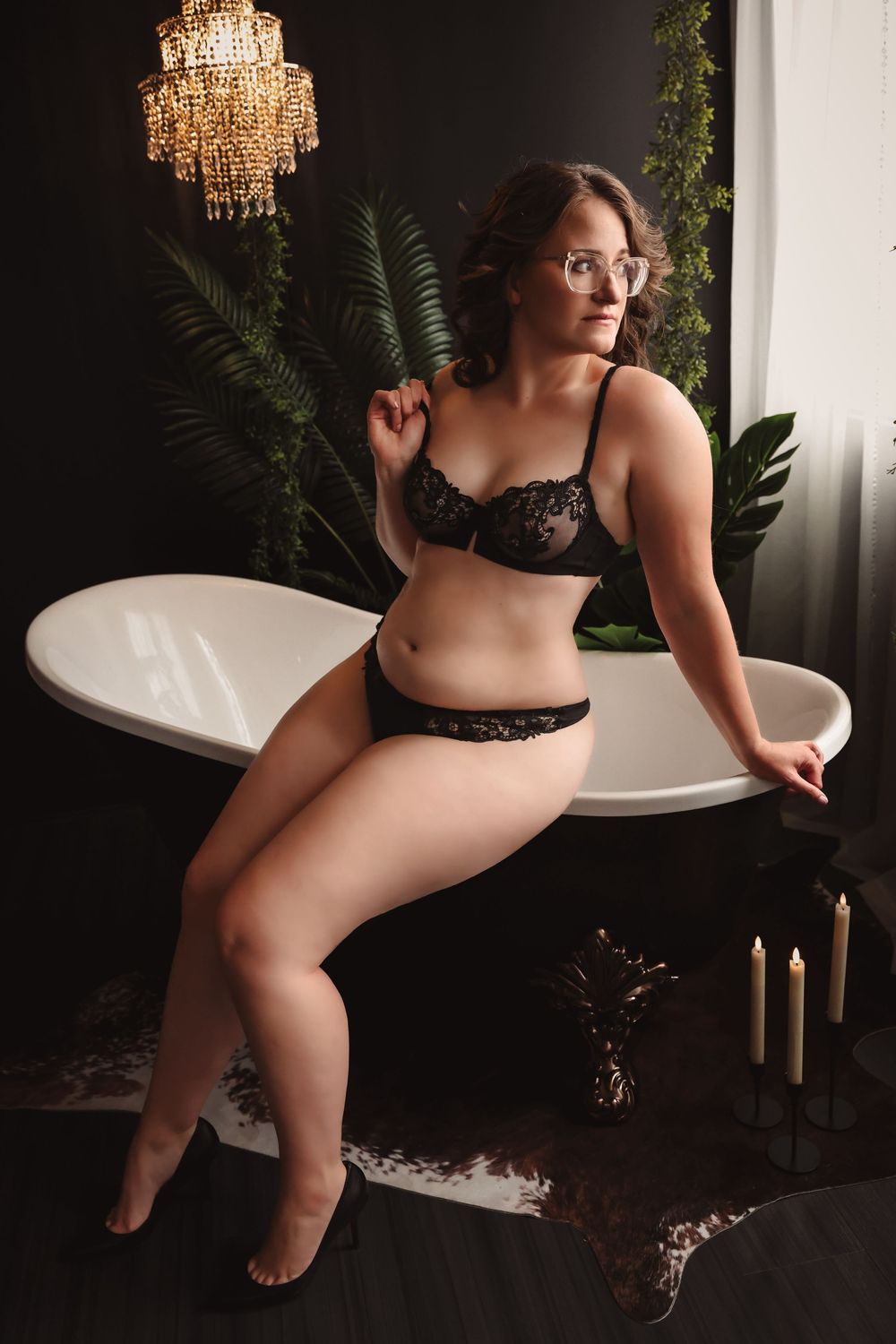 Boudoir photo featuring black lace lingerie in a moody setting with crystal chandelier and ferns.