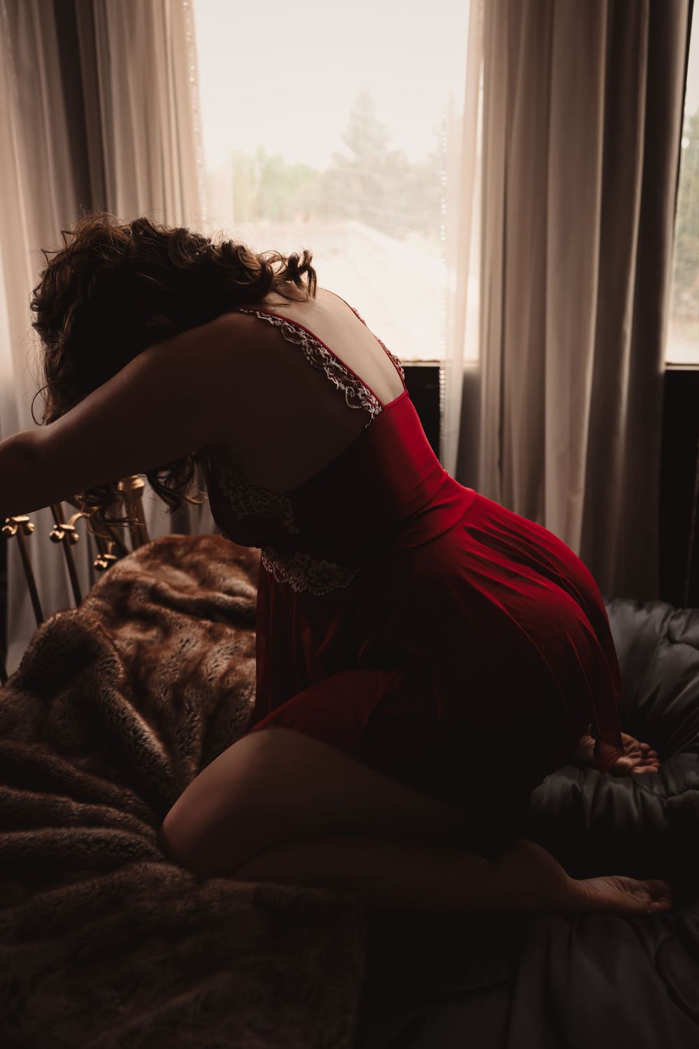A silhouette of a woman in a red dress reclines on a plush fur blanket near a window with soft lighting.