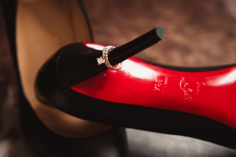 Close-up detail of a black velvet Mary Jane shoe strap against a shiny red patent leather shoe.