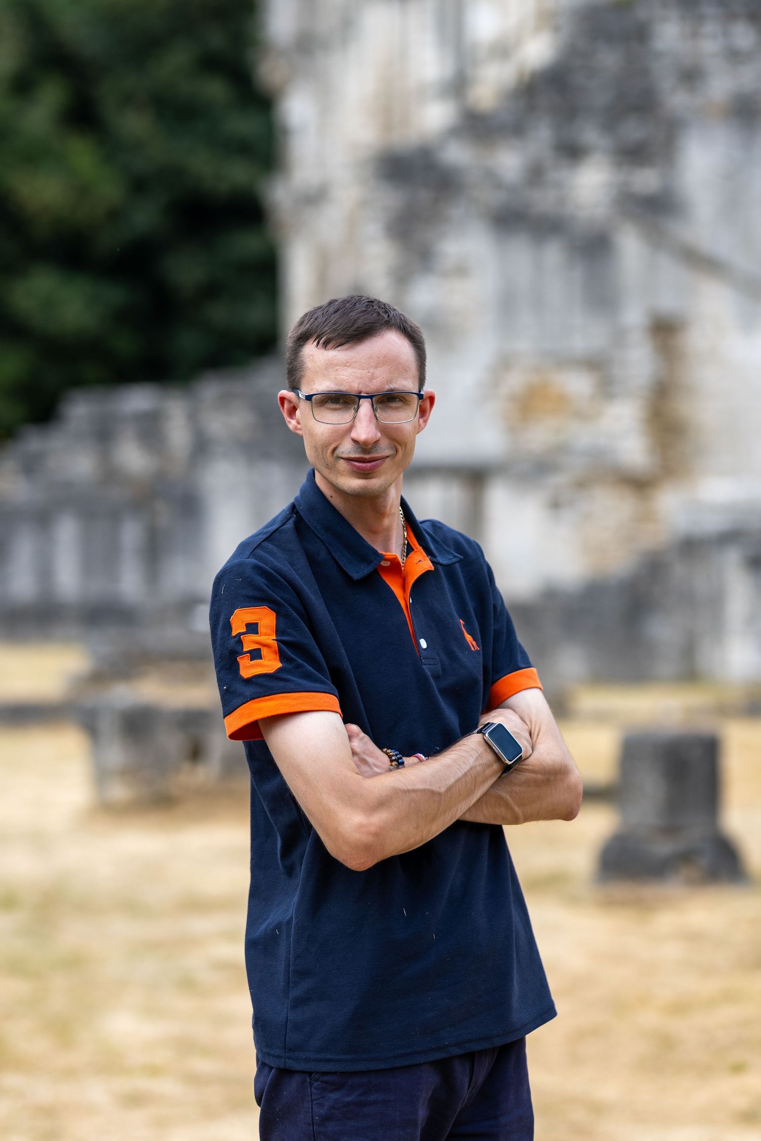 Person wearing orange jacket and glasses smiles while exploring city streets.