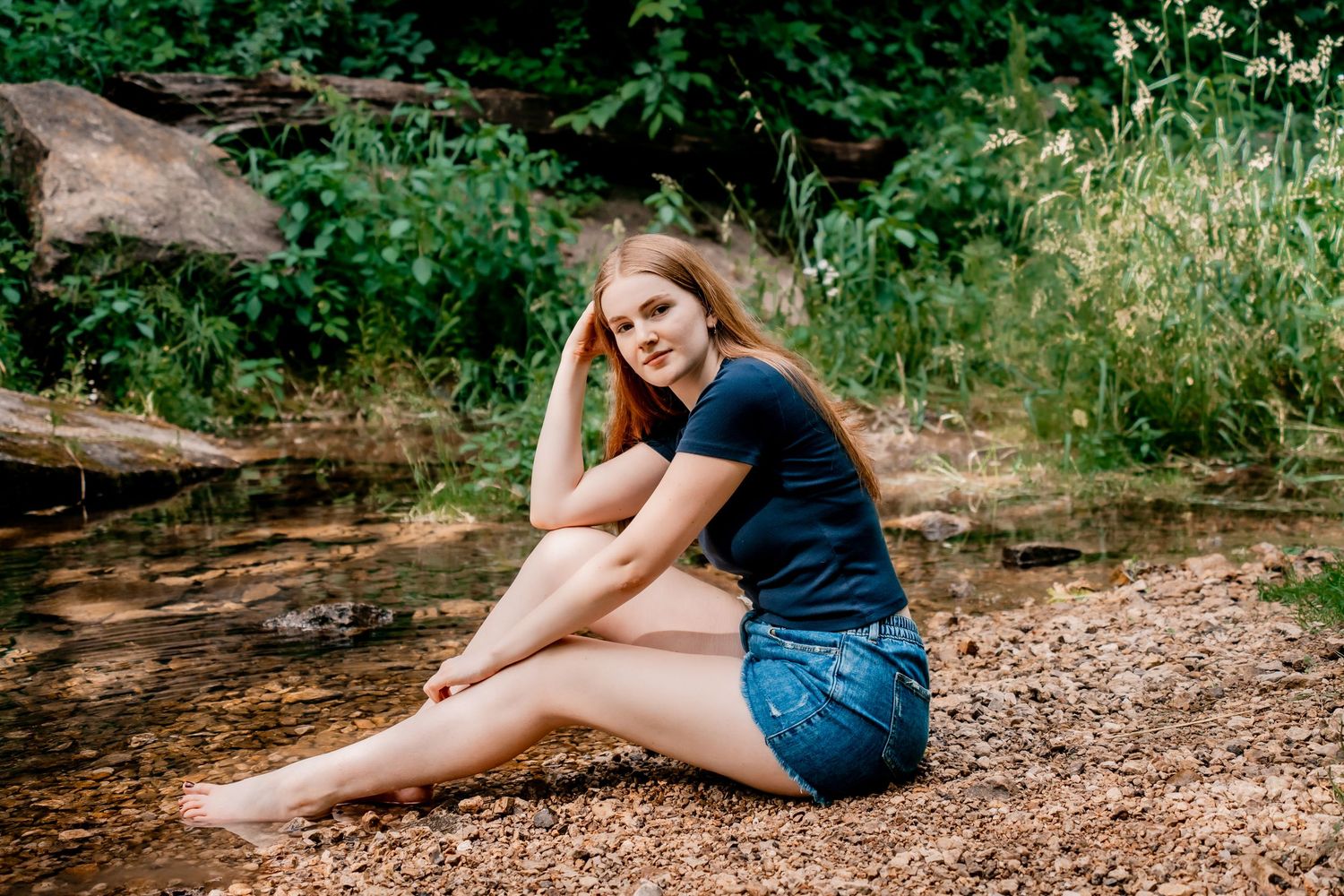 Person relaxing on a wooded trail surrounded by lush greenery and dappled sunlight.