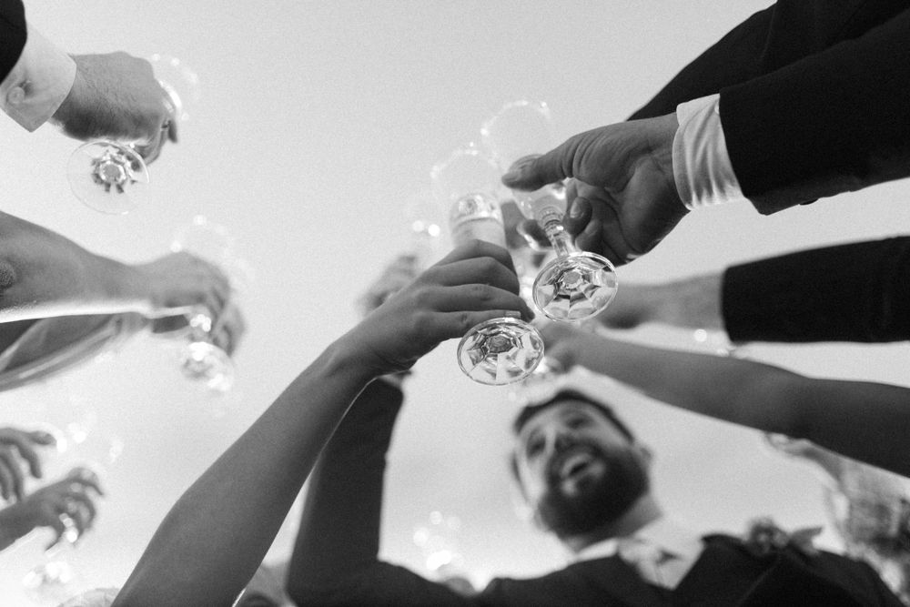 Low angle view of hands toasting with champagne glasses against bright sky.
