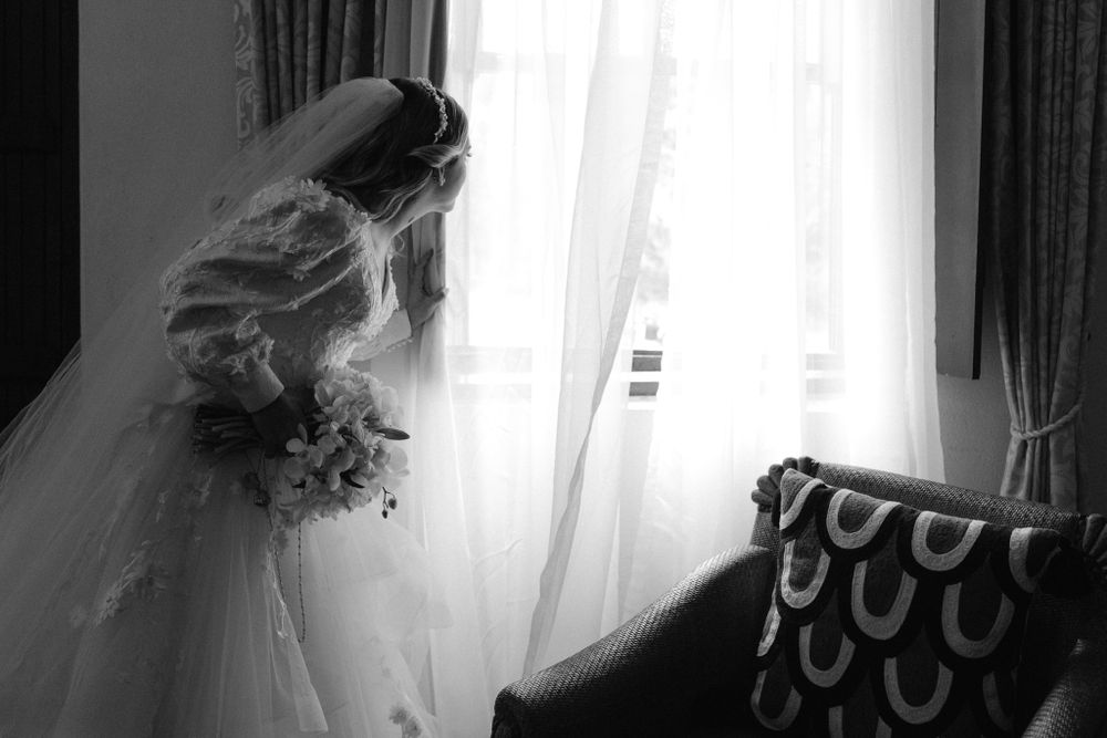 Silhouette of bride in wedding dress looking through sheer curtains.
